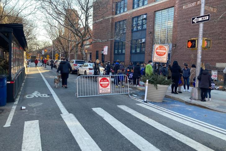 The open street barriers with "do not enter signs" outside of a school, with children and adults outside
